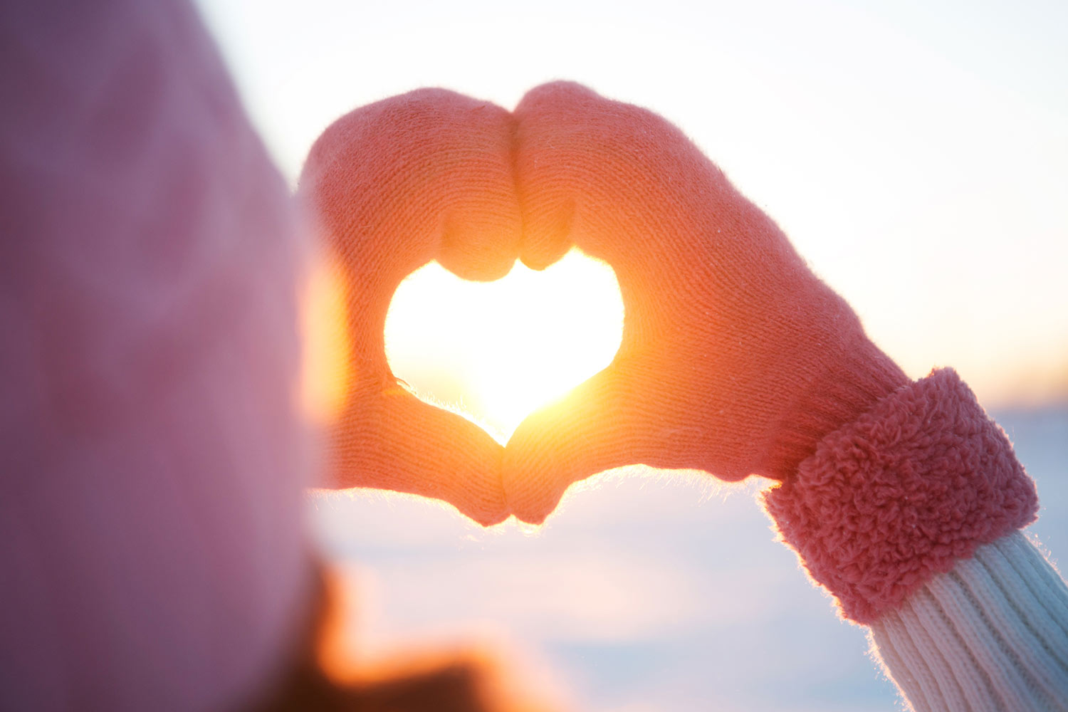 MIttened hands in a shape of a heart over a sunrise sun