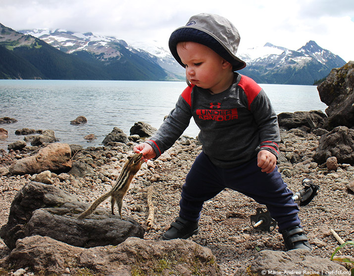 little boy feeding squirrel by lake