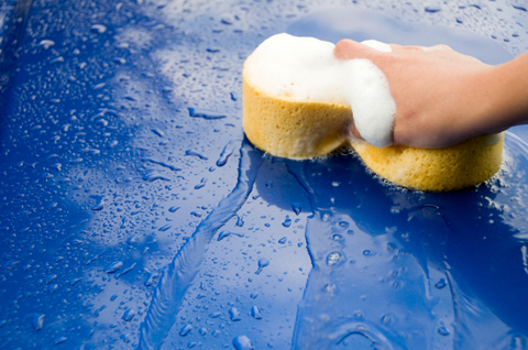 Hand sponge washing a blue car
